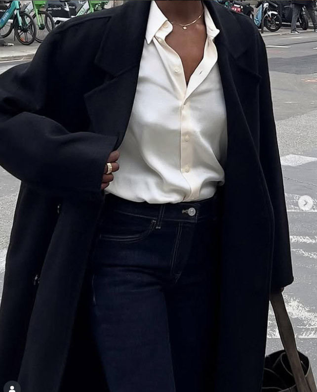 Ilgas tamsus paltas, balti marškiniai ir tamsūs prigludę džinsai – minimalistinis rudens stilius.