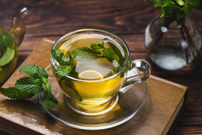 Puodelis karštos pipirmėčių arbatos su šviežiomis mėtomis – natūrali priemonė atsipalaidavimui ir peršalimui lengvinti.